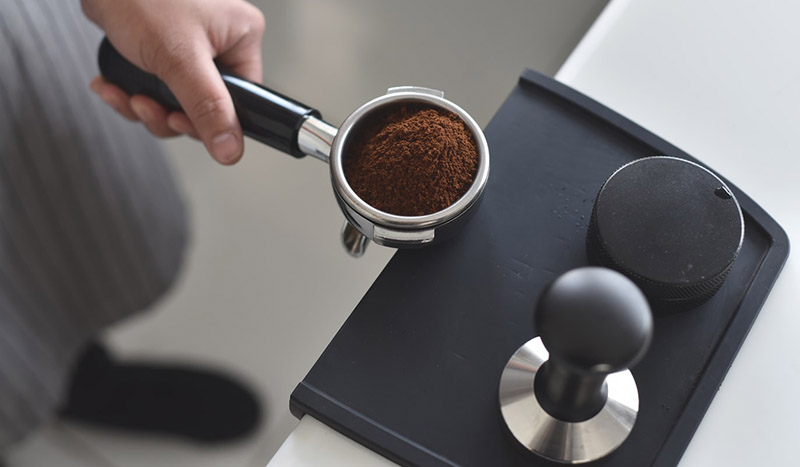 Man holding ground coffee in espresso machine coffee ground container
