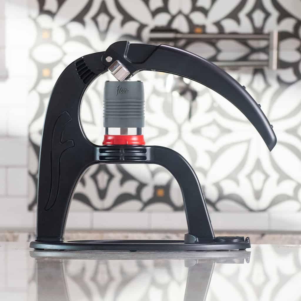 Flair NEO Flex manual direct-lever espresso maker in matte black on a countertop — all-manual polymer-frame lever mechanism with brewing cylinder and red flow-control silicone gasket visible, no motor, no battery.