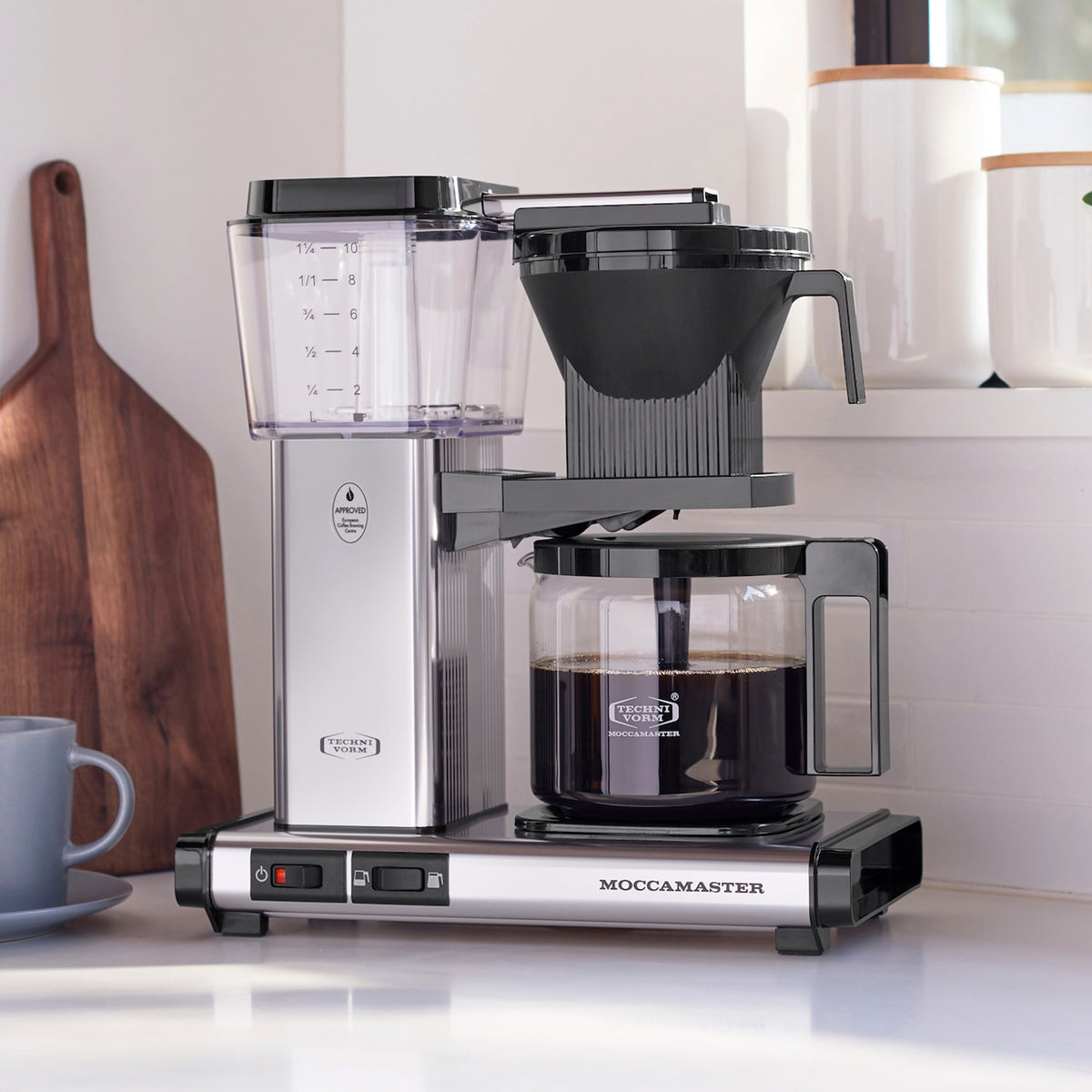 Technivorm Moccamaster KBGV Select 53941 in polished silver — copper heating element housed in the tower, glass carafe with fresh brew on the hot plate, brew basket suspended above the carafe, staged on a light kitchen counter.