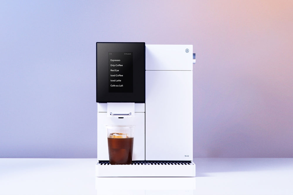 Terra Kaffe TK-02 fully automatic espresso machine in white — vertical touchscreen showing Espresso, Drip Coffee, Red Eye, Iced Coffee, Iced Latte, and Café au Lait options, iced coffee dispensing into a clear glass.